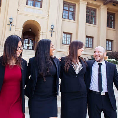 Four well dressed professionals walk on UCR's campus with interlocked arms.