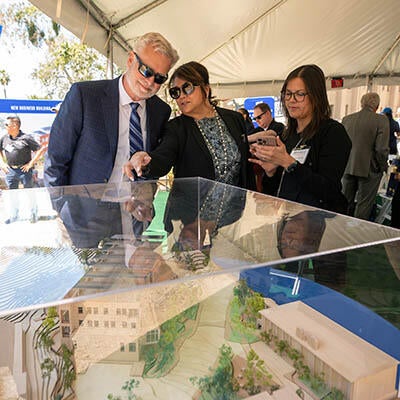 Three well dressed people stand over a model of a building.
