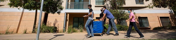Students move some items on a cart into a building at UC Riverside.