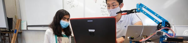 Two technicians work on a computer connected to a robot.