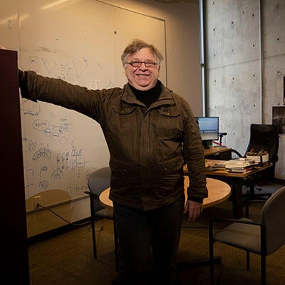 A smiling man stands in front of a desk and computer.